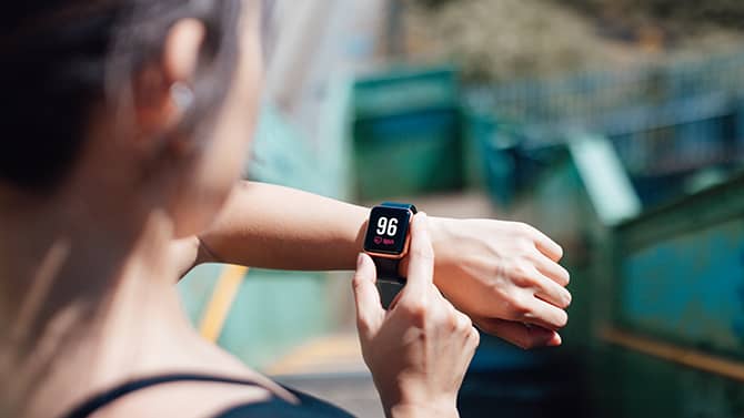 Une femme utilise une application mobile sur son téléphone, synchronisée avec une montre connectée à son poignet.