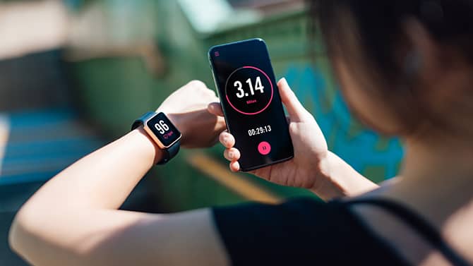 Une femme utilise une application de sport sur son smartphone et sa montre connectée. Les applications de suivi de l’activité physique sont un exemple des effets positifs que peut avoir la technologie sur la santé.